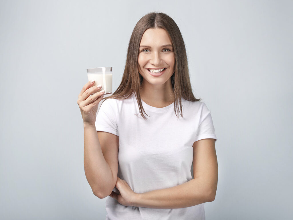 Mujer joven sonriendo con vaso de leche desnatada
