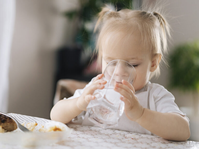 Bebé bebiendo agua de un vaso, hidratación adecuada en los niños para un desarrollo saludable