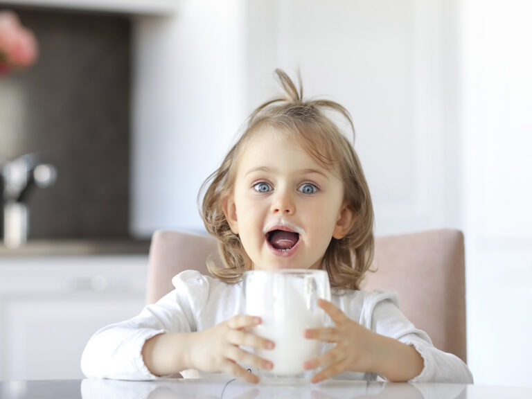 Niña feliz sosteniendo un vaso de leche, lácteos como alimento clave para el crecimiento saludable infantil