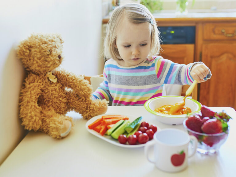 Niña comiendo sopa con verduras y frutas variadas, nutrientes esenciales en la alimentación infantil de 1 a 3 años