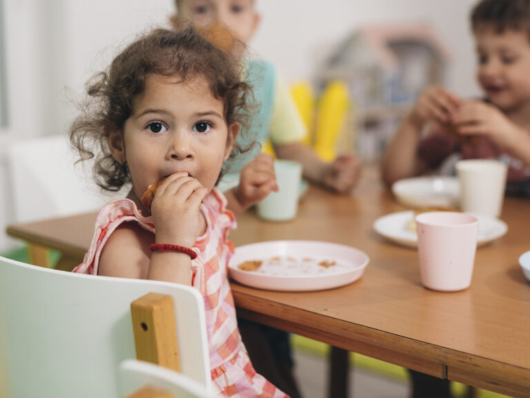 Niña comiendo en comedor escolar con otros niños