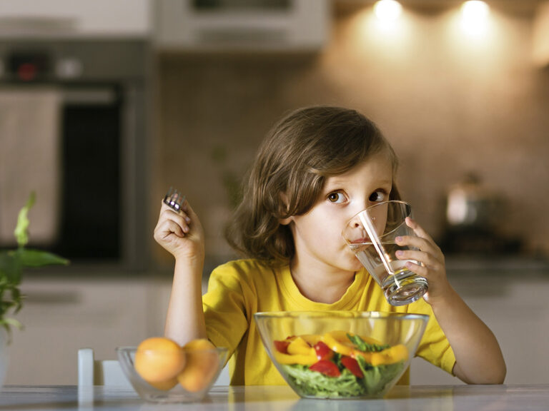 Niña bebiendo agua y comiendo ensalada