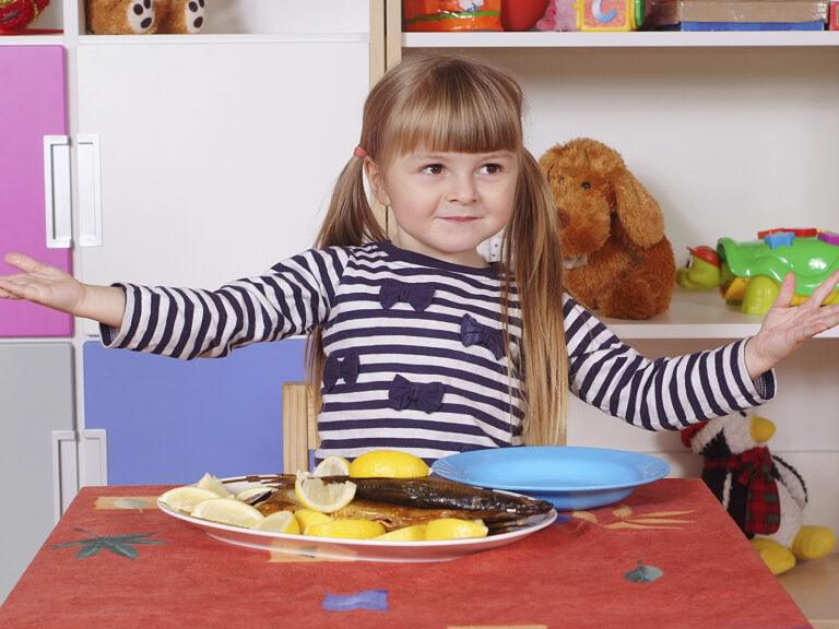 Niña comiendo pescado en plato con alimentos
