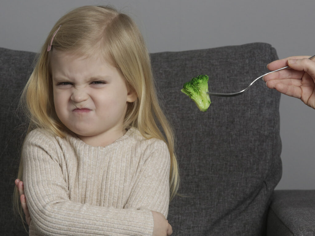 Niña rechazando el brócoli con cara de disgusto, ilustrando la alimentación selectiva y malnutrición infantil