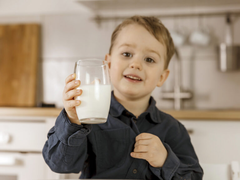Niño sonriente sosteniendo un vaso de leche en la cocina, nutrición infantil para el desarrollo cerebral