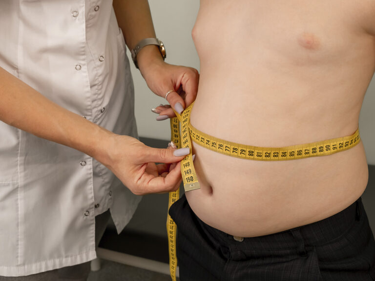 Profesional sanitario midiendo el abdomen de un niño con cinta métrica, evaluación de obesidad infantil