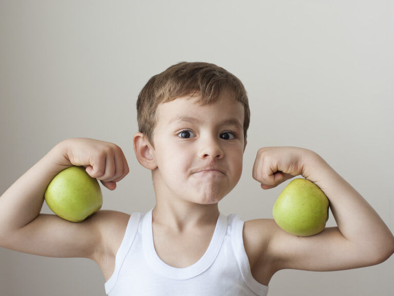 Niño fuerte presumiendo de músculos con manzanas verdes en las manos, alimentación saludable para niños deportistas