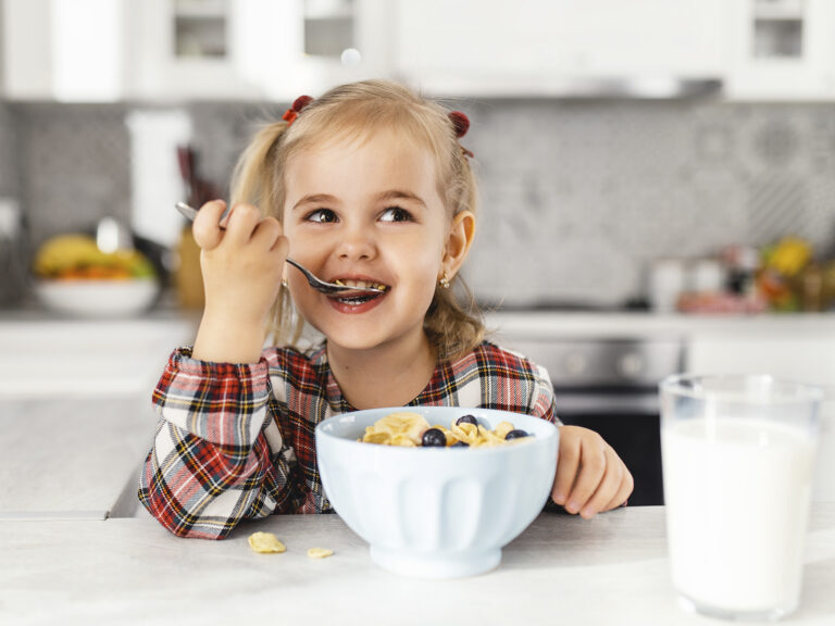 Niña sonriente desayunando un bol de cereales con leche, beneficios de un desayuno saludable