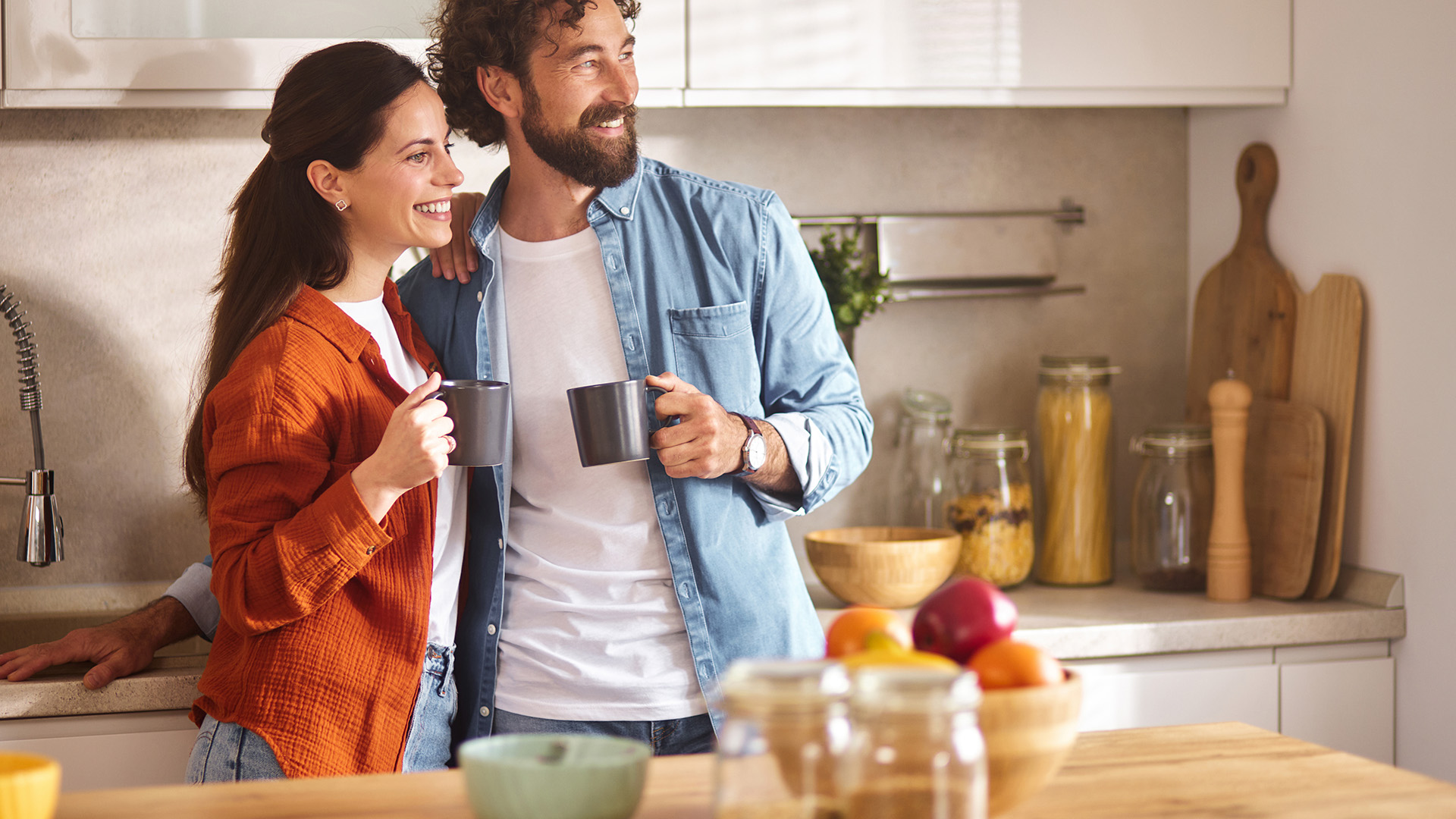 Pareja joven sonriendo con tazas en cocina moderna