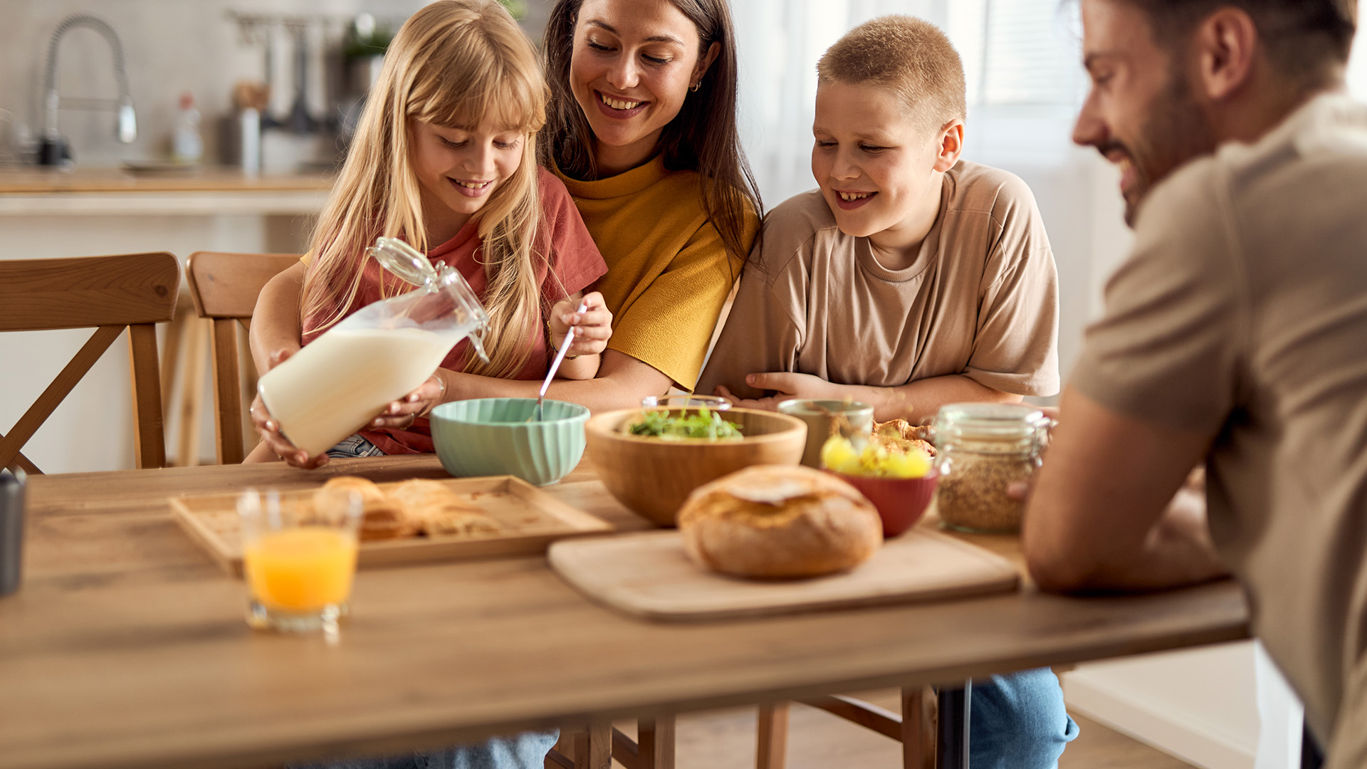 Familia desayunando juntos vertiendo leche en cuenco con frutas y pan