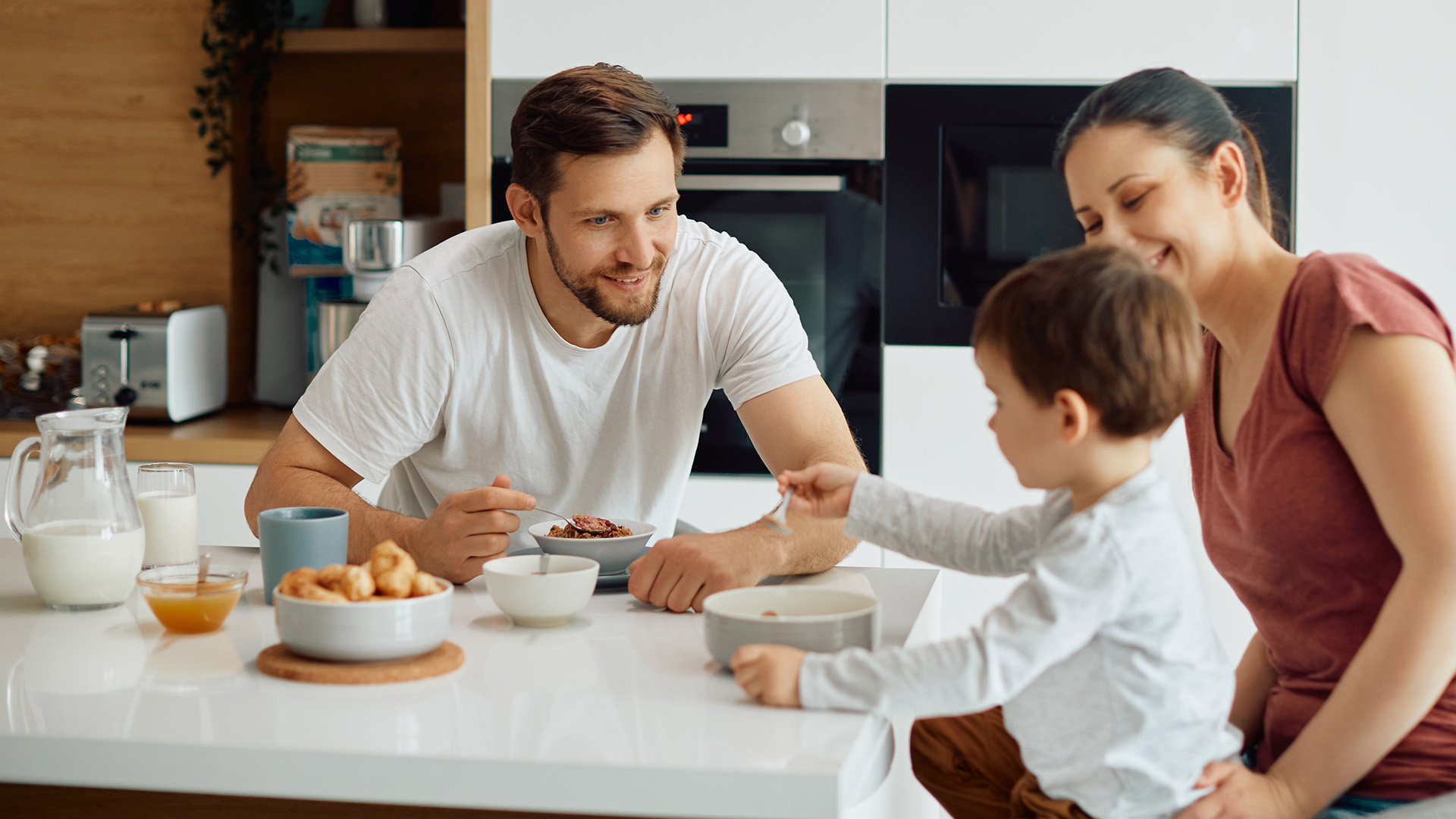 Padre madre e hijo desayunando juntos en cocina con cereales y leche
