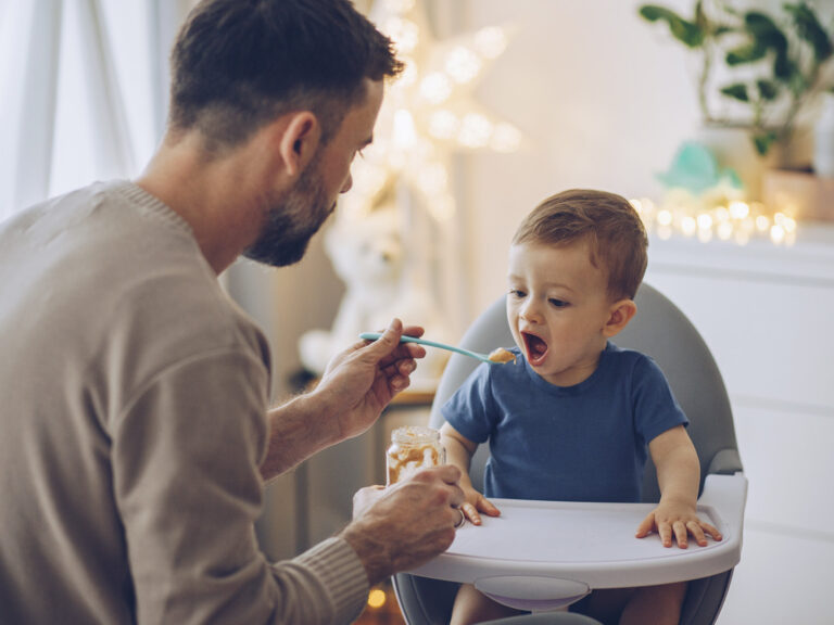 Padre alimentando con cuchara a su bebé en la trona, introducción de los potitos en la alimentación infantil