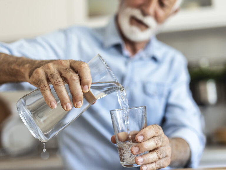 Hombre adulto vertiendo agua en vaso hidratación