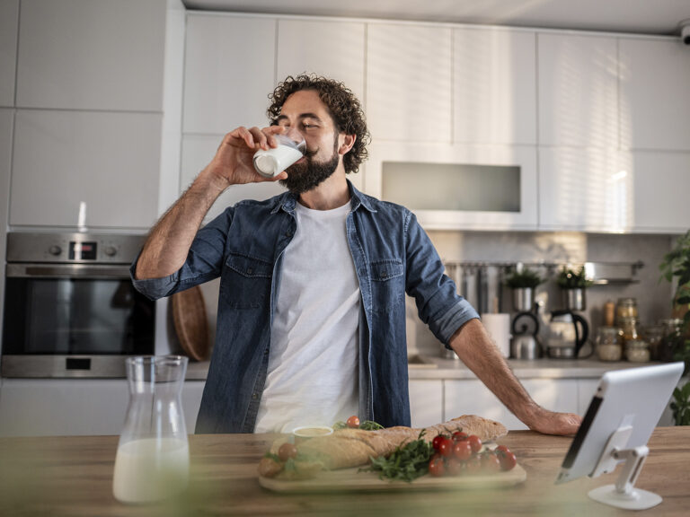 Hombre bebiendo leche en cocina con alimentos saludables