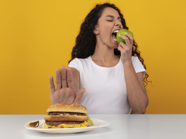 Mujer joven comiendo manzana y rechazando hamburguesa