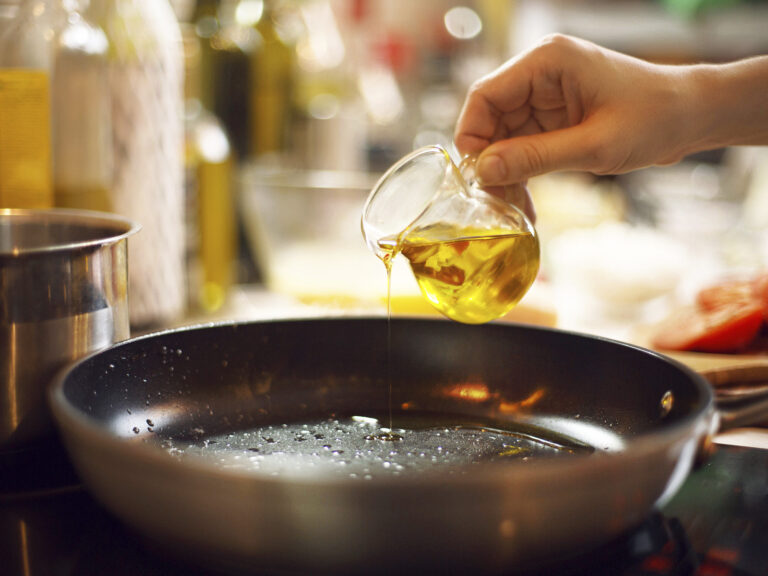 Mano vertiendo aceite de oliva en sartén