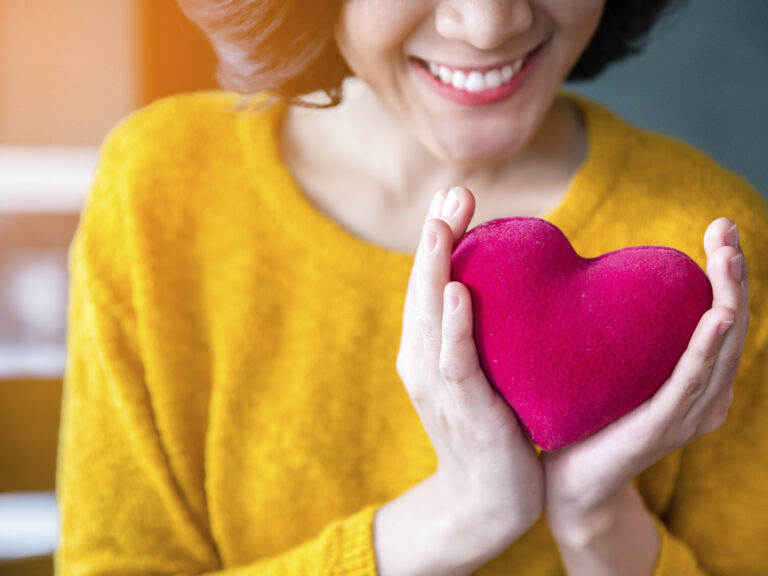Mujer sonriente sosteniendo corazón rojo representando salud