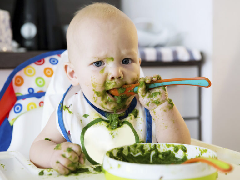 Bebé pequeño comiendo papilla de vegetales verdes con las manos y cuchara - Alimentación con puré de verduras