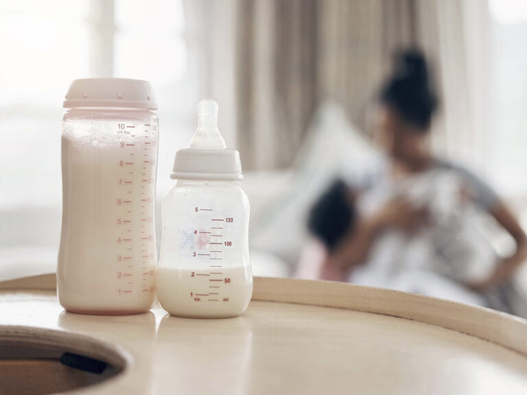 Dos biberones con leche y medidas en mililitros con madre y bebé desenfocados de fondo - Preparación de fórmula infantil