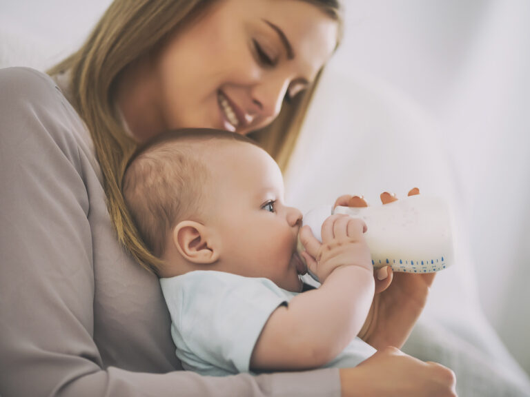 Madre sonriente sosteniendo a su bebé en brazos mientras le da el biberón de leche de continuación líquida, reflejando el vínculo maternal durante la alimentación