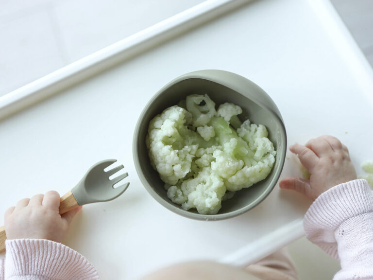 Bebé comiendo coliflor con cuchara de silicona en cuenco de alimentación
