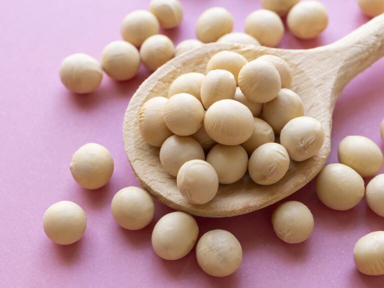 Granos de soja en cuchara de madera sobre fondo rosa